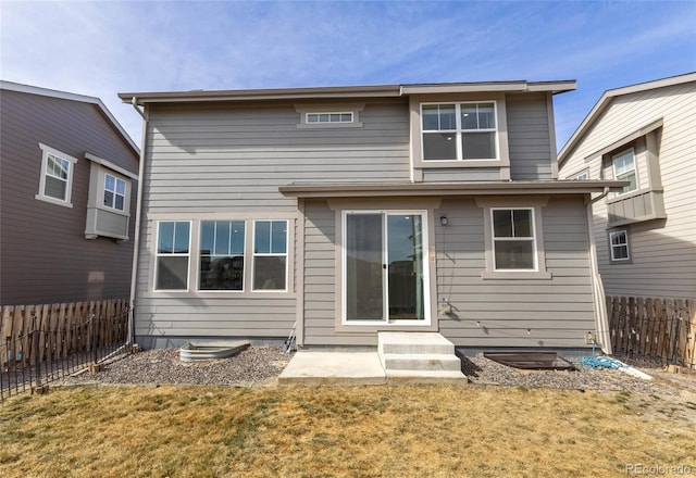 rear view of house featuring entry steps, fence, and a lawn