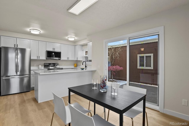 kitchen with sink, a textured ceiling, light hardwood / wood-style flooring, appliances with stainless steel finishes, and white cabinets