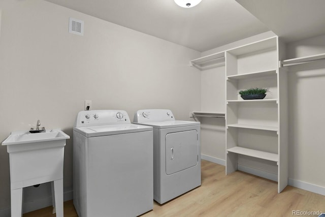 laundry area with sink, washer and dryer, and light hardwood / wood-style flooring