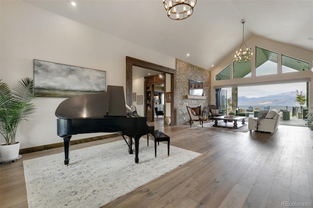 miscellaneous room with a notable chandelier, high vaulted ceiling, a stone fireplace, and wood-type flooring