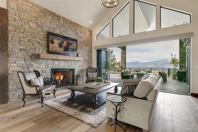 living room with a stone fireplace, a mountain view, a healthy amount of sunlight, and high vaulted ceiling