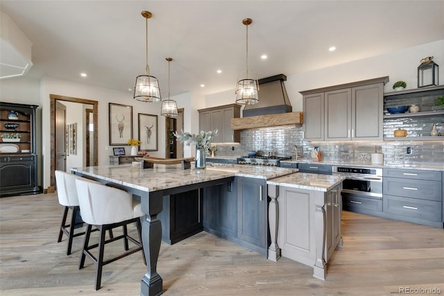 kitchen with a spacious island, custom range hood, stainless steel oven, and hanging light fixtures