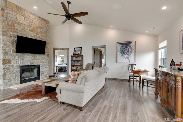 living room featuring a stone fireplace, high vaulted ceiling, light wood-type flooring, and ceiling fan