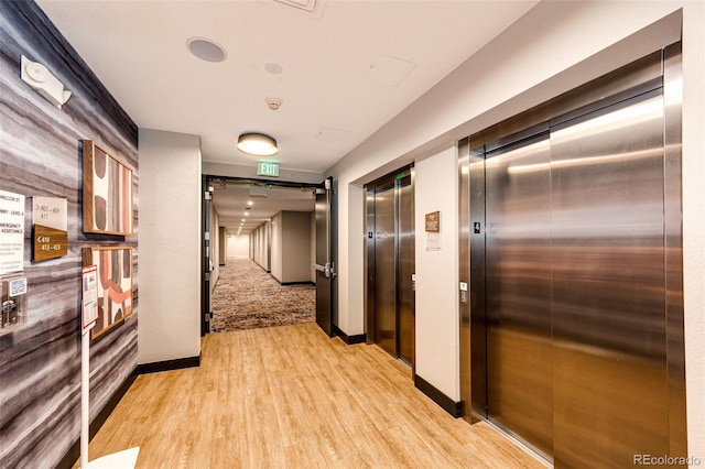 hallway with elevator and light hardwood / wood-style flooring