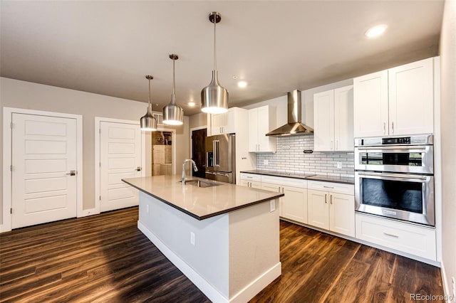 kitchen featuring dark hardwood / wood-style floors, pendant lighting, wall chimney range hood, and appliances with stainless steel finishes