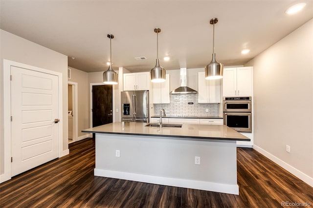 kitchen with white cabinets, wall chimney range hood, sink, an island with sink, and stainless steel appliances