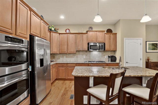 8582 E 148th Ln, Thornton, CO 80602 - kitchen with stainless steel appliances, light wood-style floors, decorative backsplash, light stone counters, and a kitchen breakfast bar