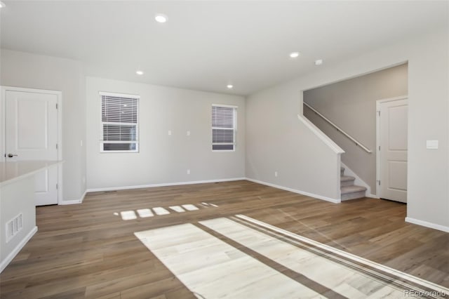 empty room featuring recessed lighting, visible vents, wood finished floors, baseboards, and stairs