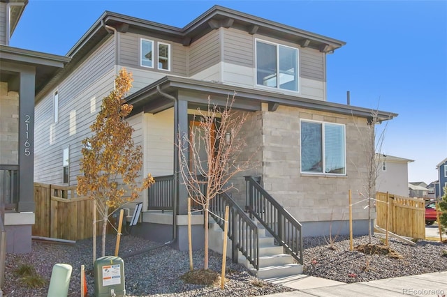 view of front of house featuring entry steps, stone siding, and fence