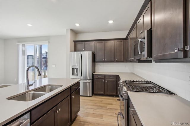 kitchen featuring stainless steel appliances, dark brown cabinets, light countertops, light wood-style floors, and a sink