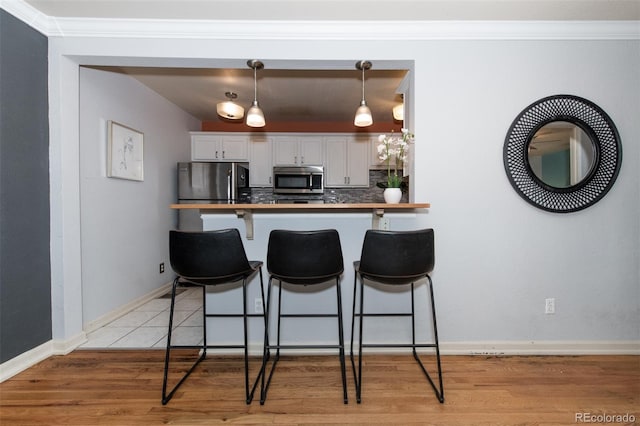 kitchen with light wood-type flooring, appliances with stainless steel finishes, tasteful backsplash, decorative light fixtures, and white cabinetry