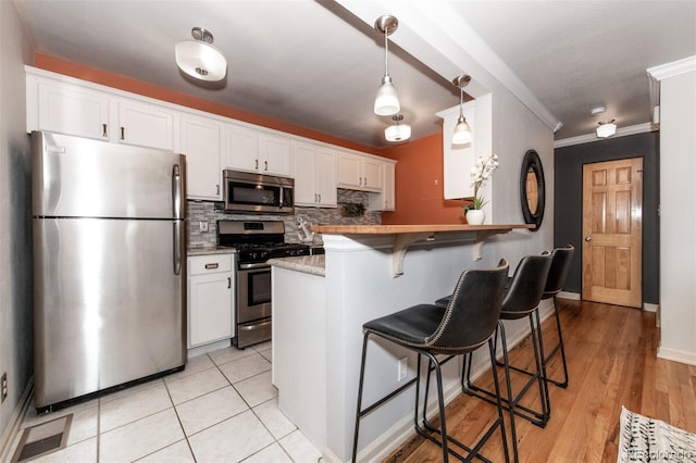 kitchen with a kitchen breakfast bar, kitchen peninsula, white cabinetry, and stainless steel appliances