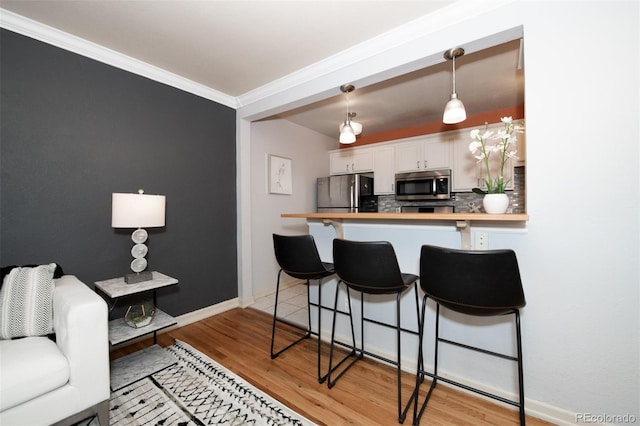 kitchen with white cabinets, hanging light fixtures, decorative backsplash, appliances with stainless steel finishes, and a kitchen bar