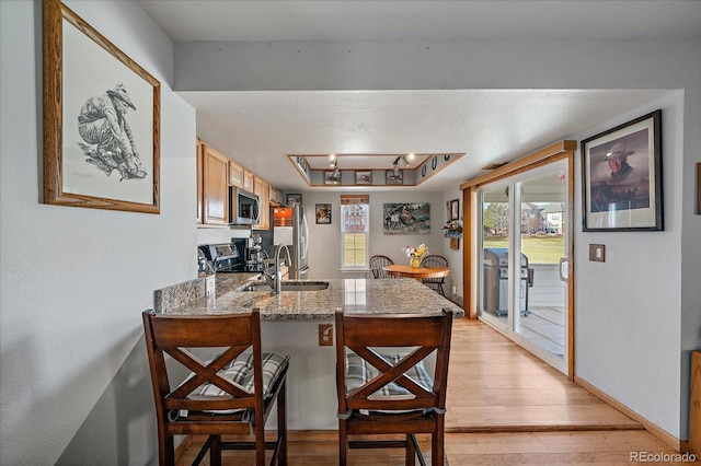 kitchen with stainless steel appliances, stone counters, a raised ceiling, light hardwood / wood-style floors, and kitchen peninsula