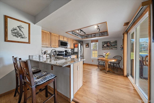 kitchen with a raised ceiling, a breakfast bar area, appliances with stainless steel finishes, kitchen peninsula, and dark stone counters