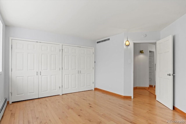 550 E 12th Ave Unit 209, Denver, CO 80203 - unfurnished bedroom with light wood-style flooring, two closets, baseboards, and a baseboard heating unit