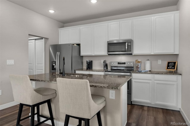 kitchen with dark stone counters, a center island with sink, white cabinets, appliances with stainless steel finishes, and dark hardwood / wood-style flooring