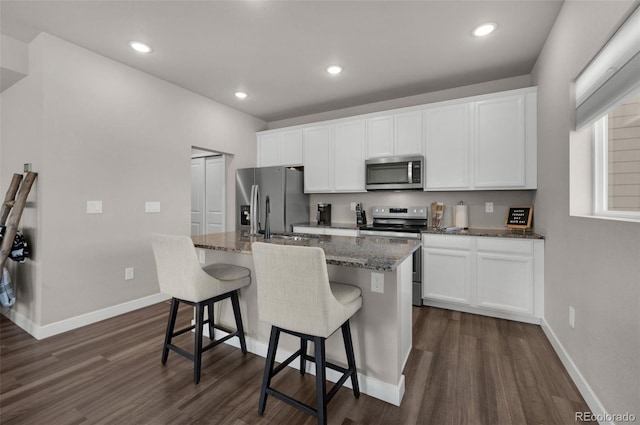 kitchen with appliances with stainless steel finishes, dark hardwood / wood-style flooring, white cabinetry, and a kitchen island with sink