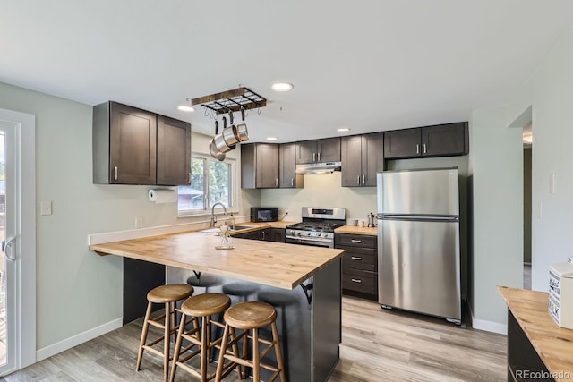 kitchen with wood counters, appliances with stainless steel finishes, a kitchen bar, and sink