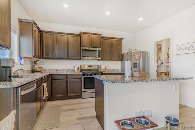 kitchen with light wood-style flooring, stainless steel appliances, a sink, and stone countertops