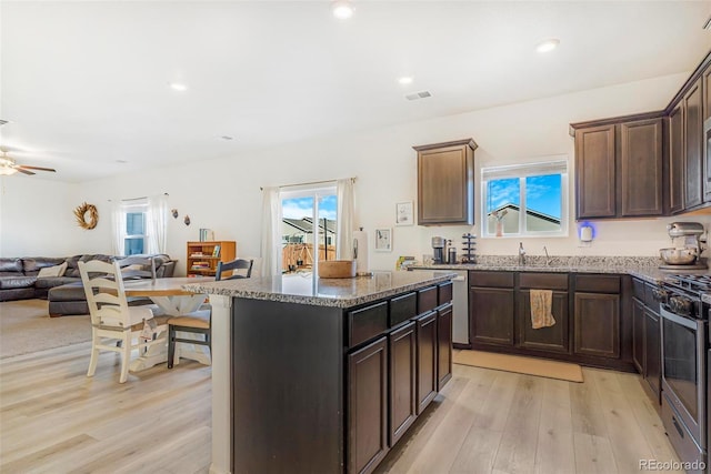 kitchen with stone countertops, light wood-style flooring, visible vents, open floor plan, and gas stove