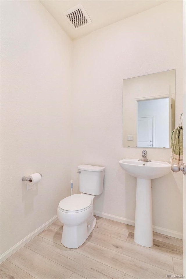 half bath featuring toilet, wood finished floors, visible vents, and baseboards