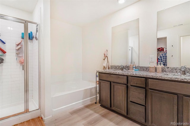 full bath featuring a stall shower, a garden tub, a sink, and wood finished floors