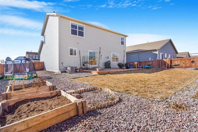 rear view of house featuring a trampoline, a vegetable garden, a lawn, central AC, and fence