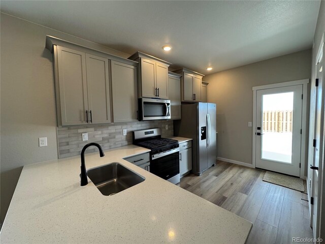 kitchen featuring light wood finished floors, gray cabinets, a sink, appliances with stainless steel finishes, and tasteful backsplash