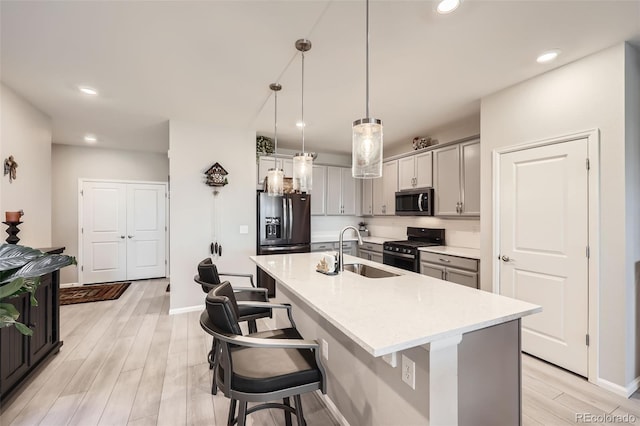 kitchen featuring a center island with sink, sink, hanging light fixtures, gray cabinets, and stainless steel appliances