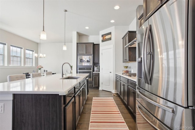 kitchen featuring appliances with stainless steel finishes, decorative light fixtures, sink, dark brown cabinets, and a center island with sink