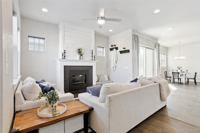 living room with a brick fireplace, ceiling fan with notable chandelier, and dark hardwood / wood-style flooring