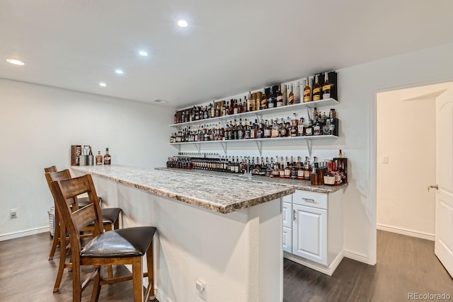 bar with dark hardwood / wood-style flooring, light stone countertops, and white cabinets