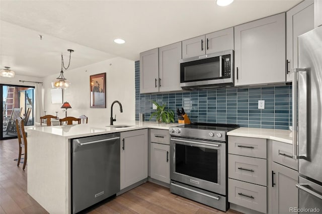 kitchen with kitchen peninsula, gray cabinets, stainless steel appliances, hanging light fixtures, and sink