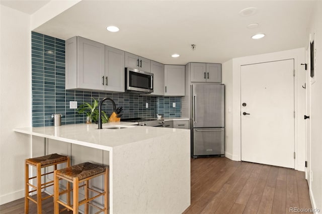 kitchen with kitchen peninsula, stainless steel appliances, gray cabinetry, dark wood-type flooring, and sink