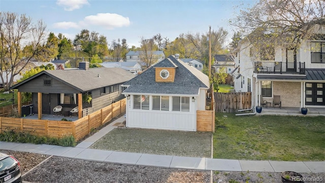view of front facade featuring a residential view, an outdoor structure, a patio area, a shingled roof, and a balcony