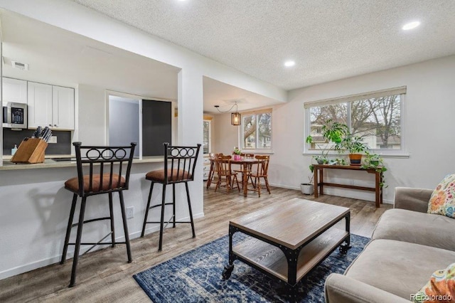 living area featuring a textured ceiling, light wood-type flooring, recessed lighting, and baseboards