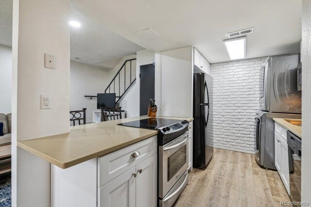 kitchen featuring black appliances, stacked washing machine and dryer, light wood-type flooring, a peninsula, and a textured ceiling