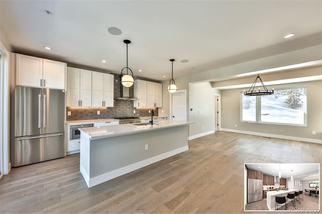 kitchen featuring appliances with stainless steel finishes, white cabinetry, hanging light fixtures, a center island with sink, and wall chimney exhaust hood