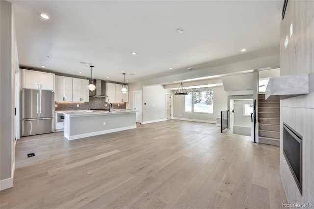 kitchen with decorative light fixtures, white cabinets, light wood-type flooring, a kitchen island with sink, and stainless steel refrigerator