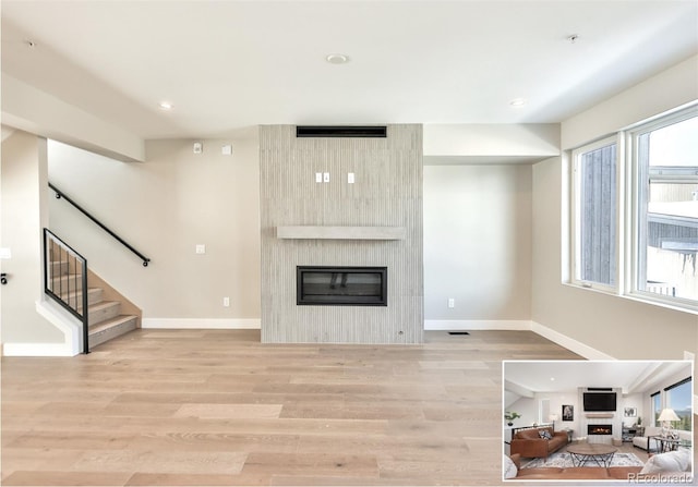 living room featuring light wood-type flooring, a healthy amount of sunlight, and a large fireplace