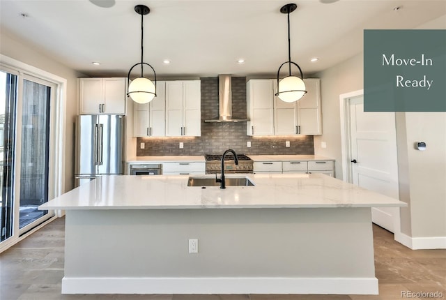 kitchen featuring wall chimney exhaust hood, a center island with sink, pendant lighting, and stainless steel appliances