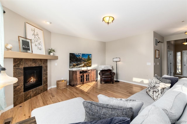 living area with baseboards, visible vents, a tiled fireplace, and wood finished floors