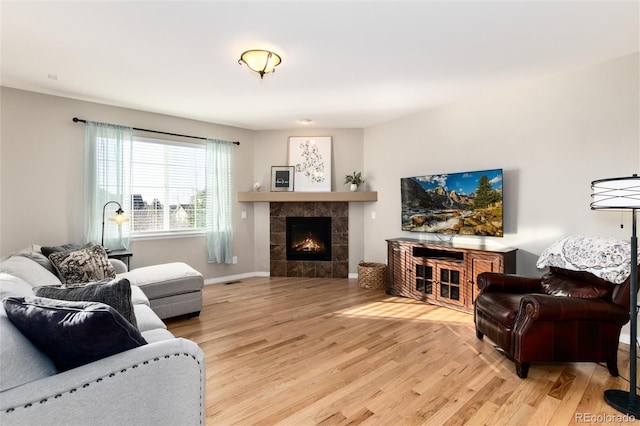 living room with light wood-type flooring, visible vents, a fireplace, and baseboards