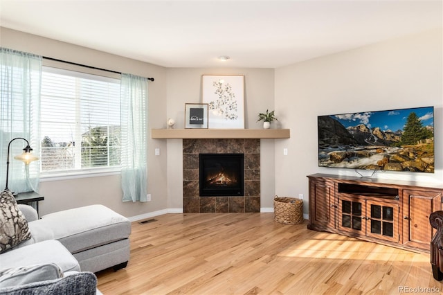 living room with a tiled fireplace, wood finished floors, visible vents, and baseboards