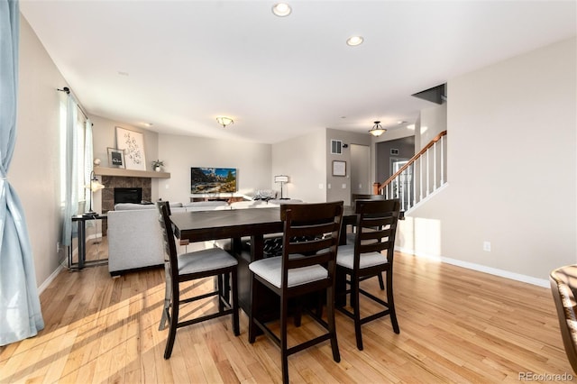 dining space featuring light wood finished floors, baseboards, stairway, and a tile fireplace