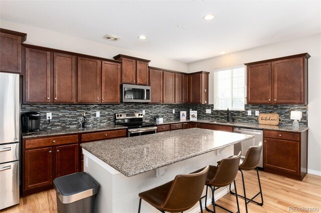 kitchen featuring a center island, stainless steel appliances, light wood-type flooring, a kitchen bar, and a sink