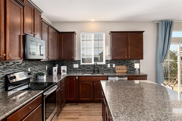 kitchen featuring light wood-style flooring, stainless steel appliances, a sink, decorative backsplash, and dark stone countertops