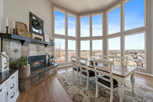 dining area with baseboards, a stone fireplace, a towering ceiling, and wood finished floors