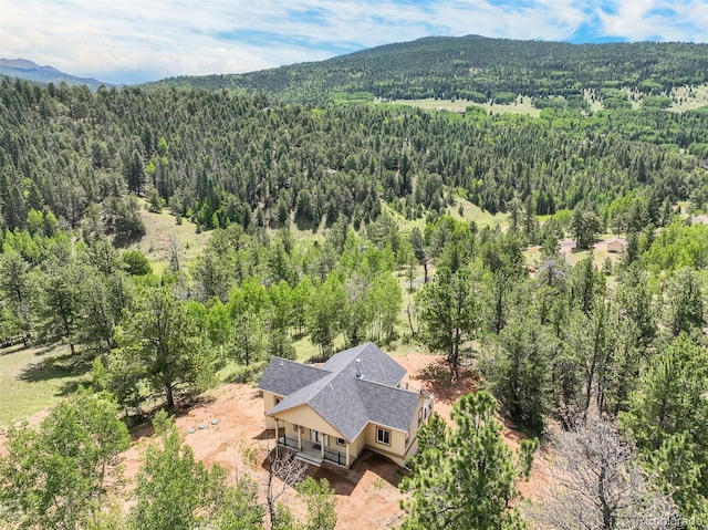 aerial view of property and surrounding area featuring a forest and a mountainous background